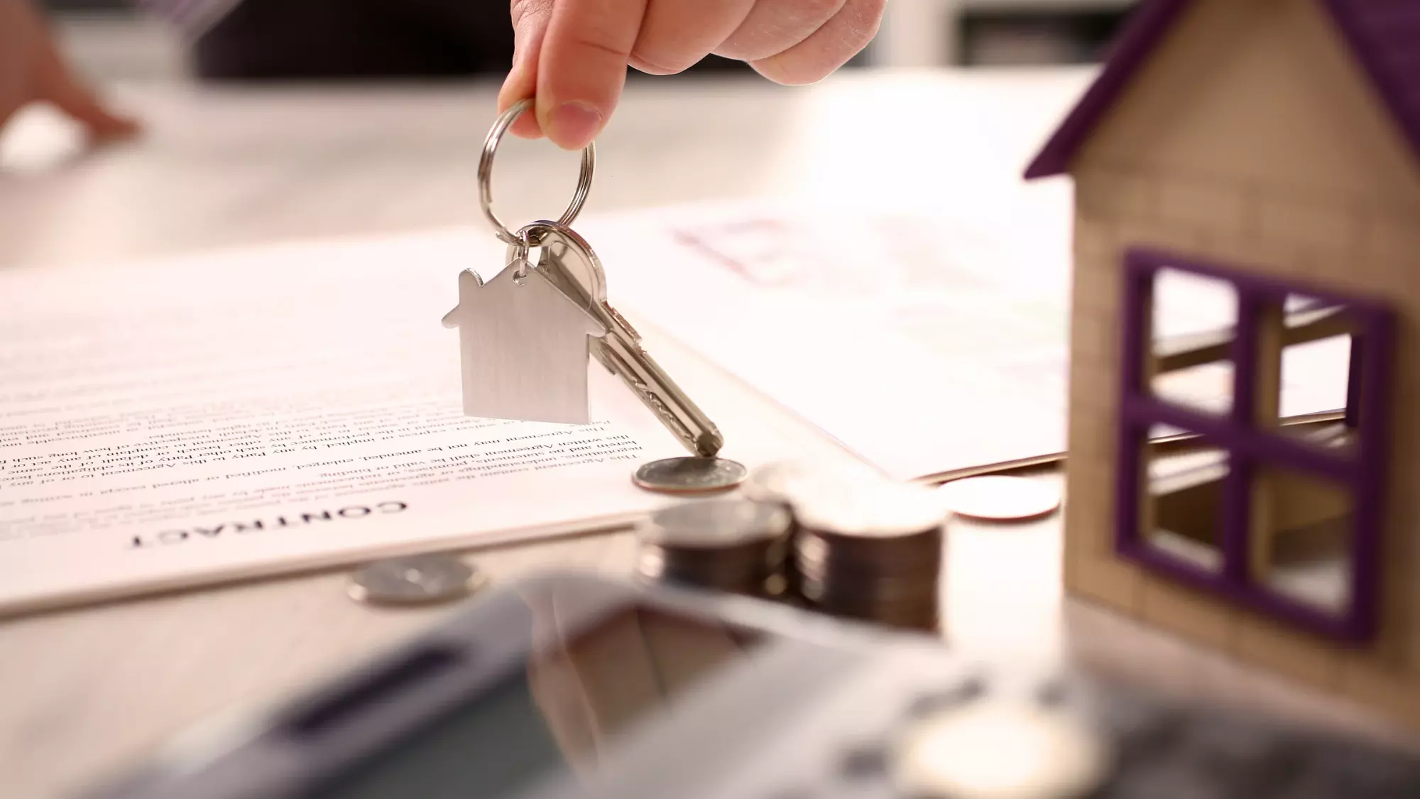 Une main qui donne les clés d'une maison, sur un bureau où sont des documents