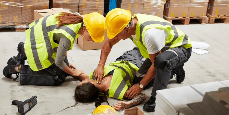 Un ouvrier victime d'un accident du travail, au sol, avec deux autres ouvriers qui lui donnent les premiers secours.